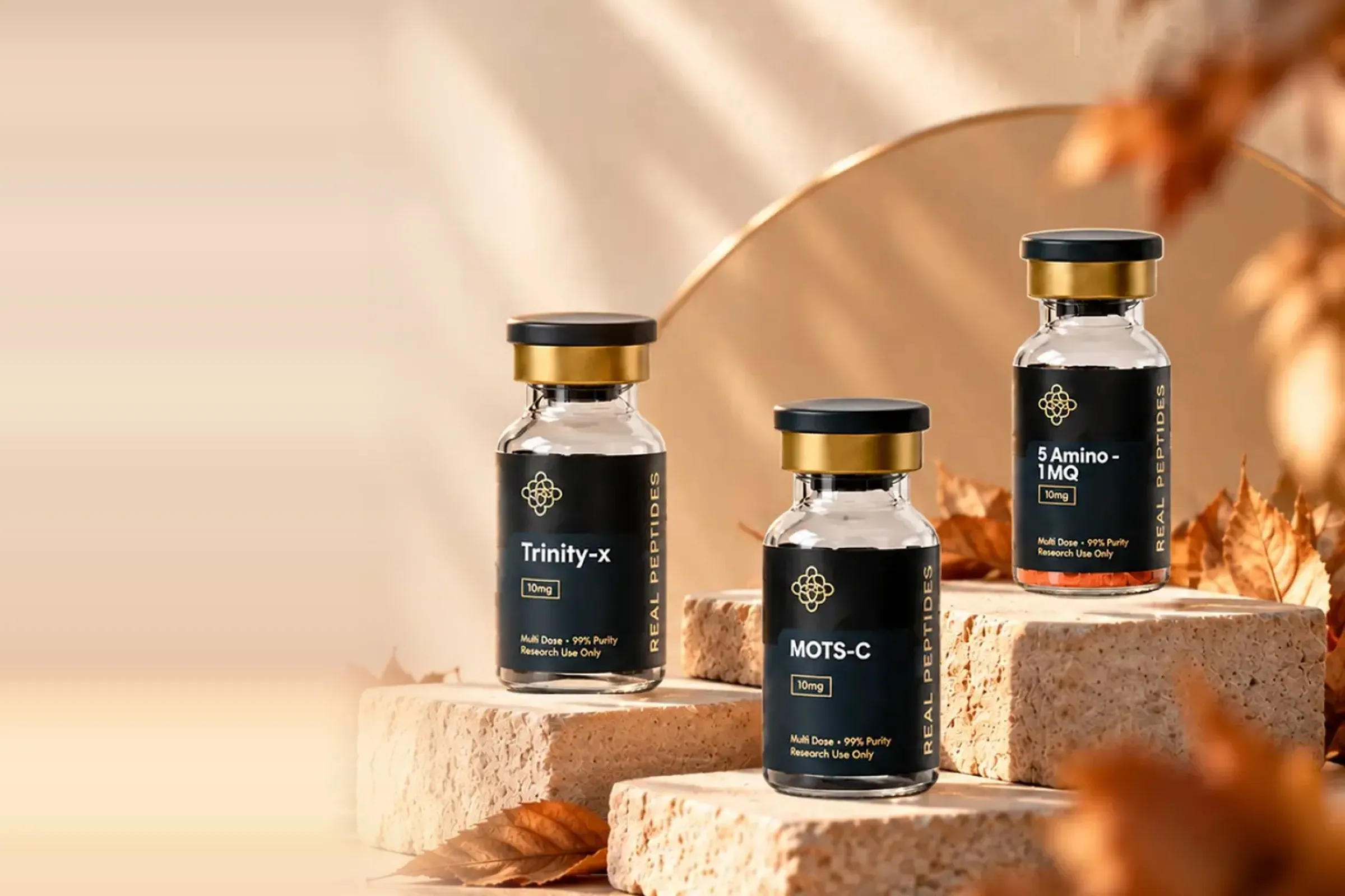 Real Peptides Trinity-X, MOTS-C and 5-Amino-1MQ vials on stone blocks in warm sunlight